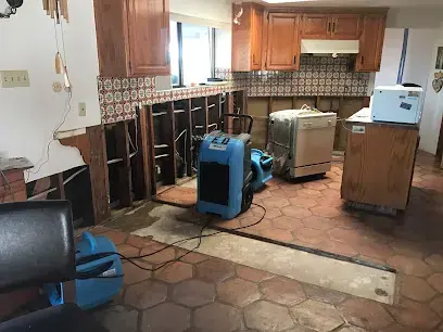 Dehumidifiers drying a Spanish-tile kitchen with the lower cabinets removed after a water loss