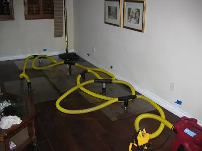 Yellow hoses and drying mats pulling water out of a dark hardwood floor