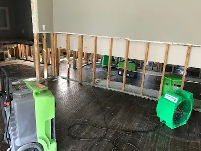 Studs exposed where a wall was cut along its base, green air movers on a dark floor