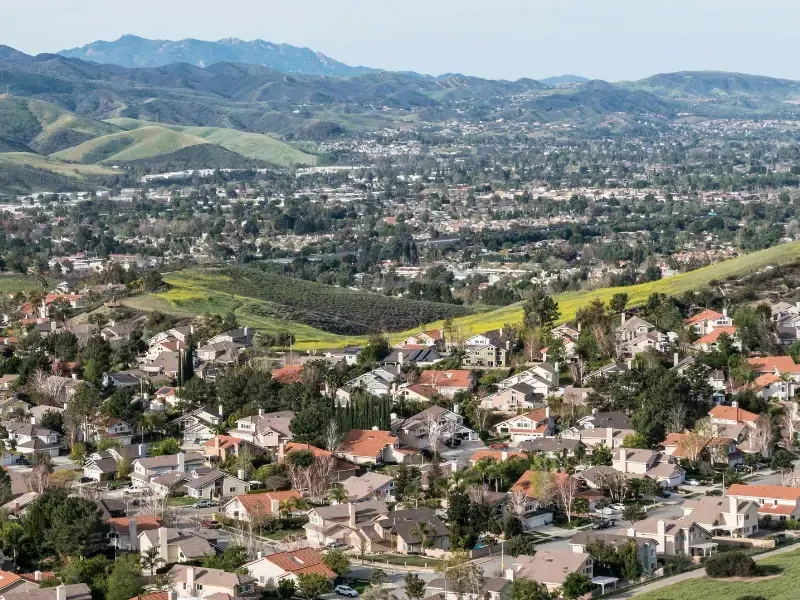 Aerial view of tile-roof homes spread across a hillside valley below green hills